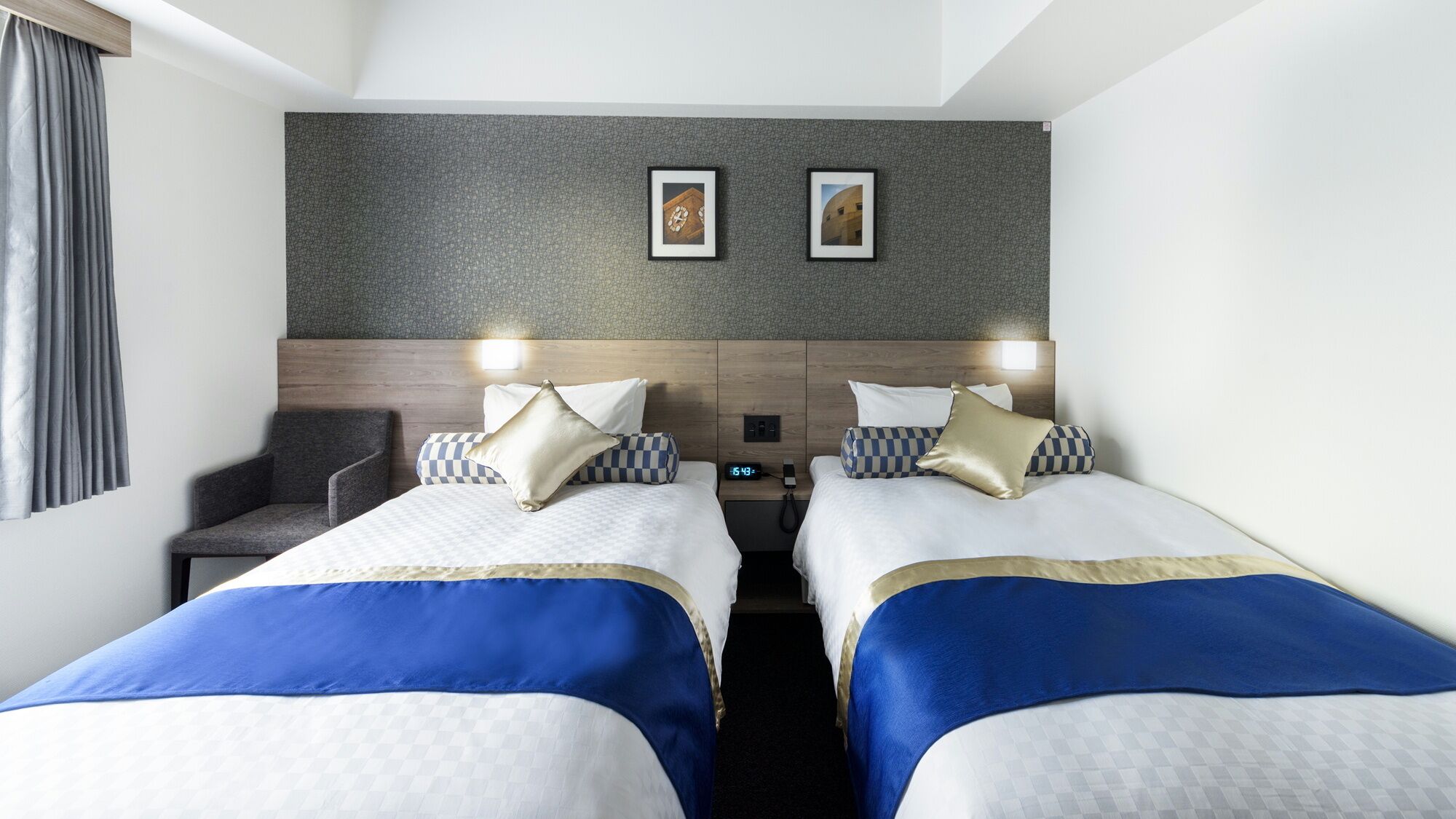 Een hotelkamer met twee bedden, een stoel, een klok en twee foto's in lijsten aan de muur.