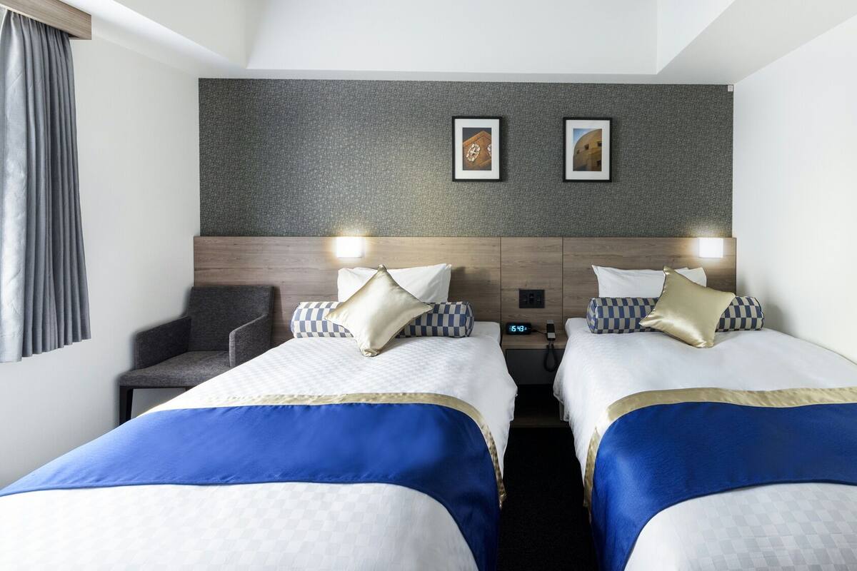 Een hotelkamer met twee bedden, een stoel, een klok en twee foto's in lijsten aan de muur.