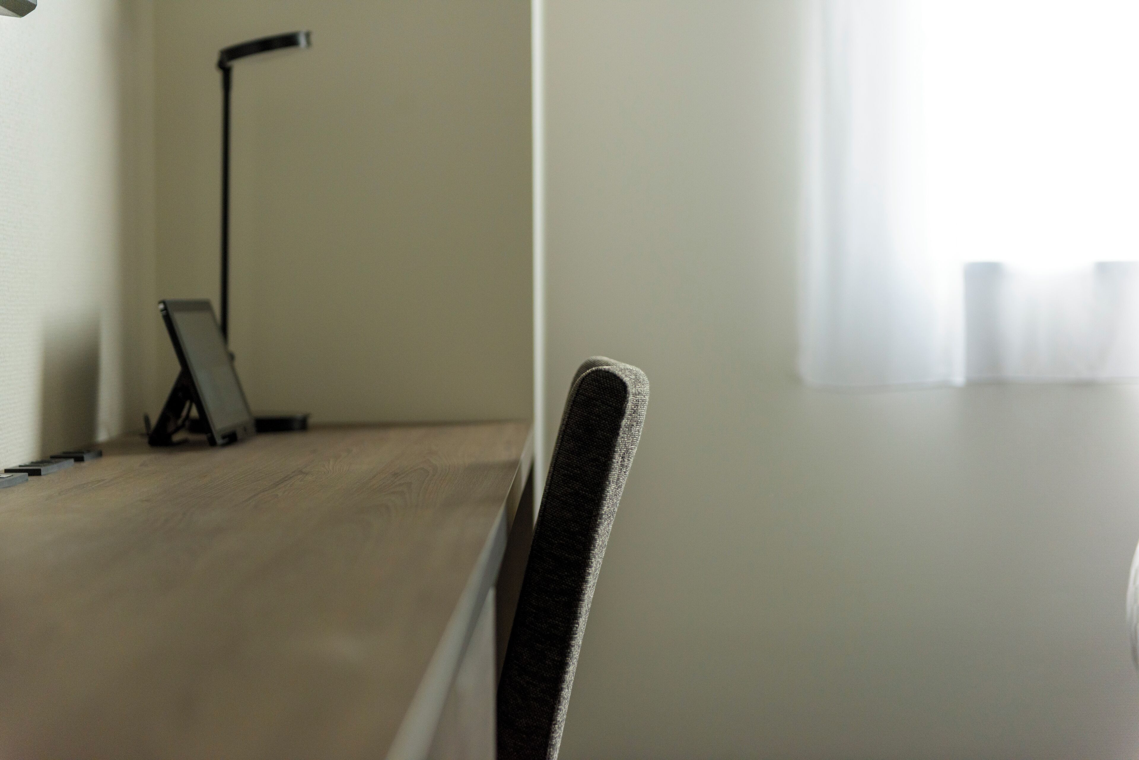 A close-up of a chair with a textured backrest, a lamp, and a window with sheer curtains.