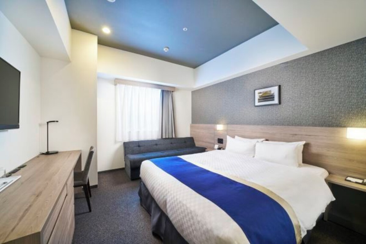 A hotel room with a large bed, a desk, a chair, a sofa, and a flat-screen TV.