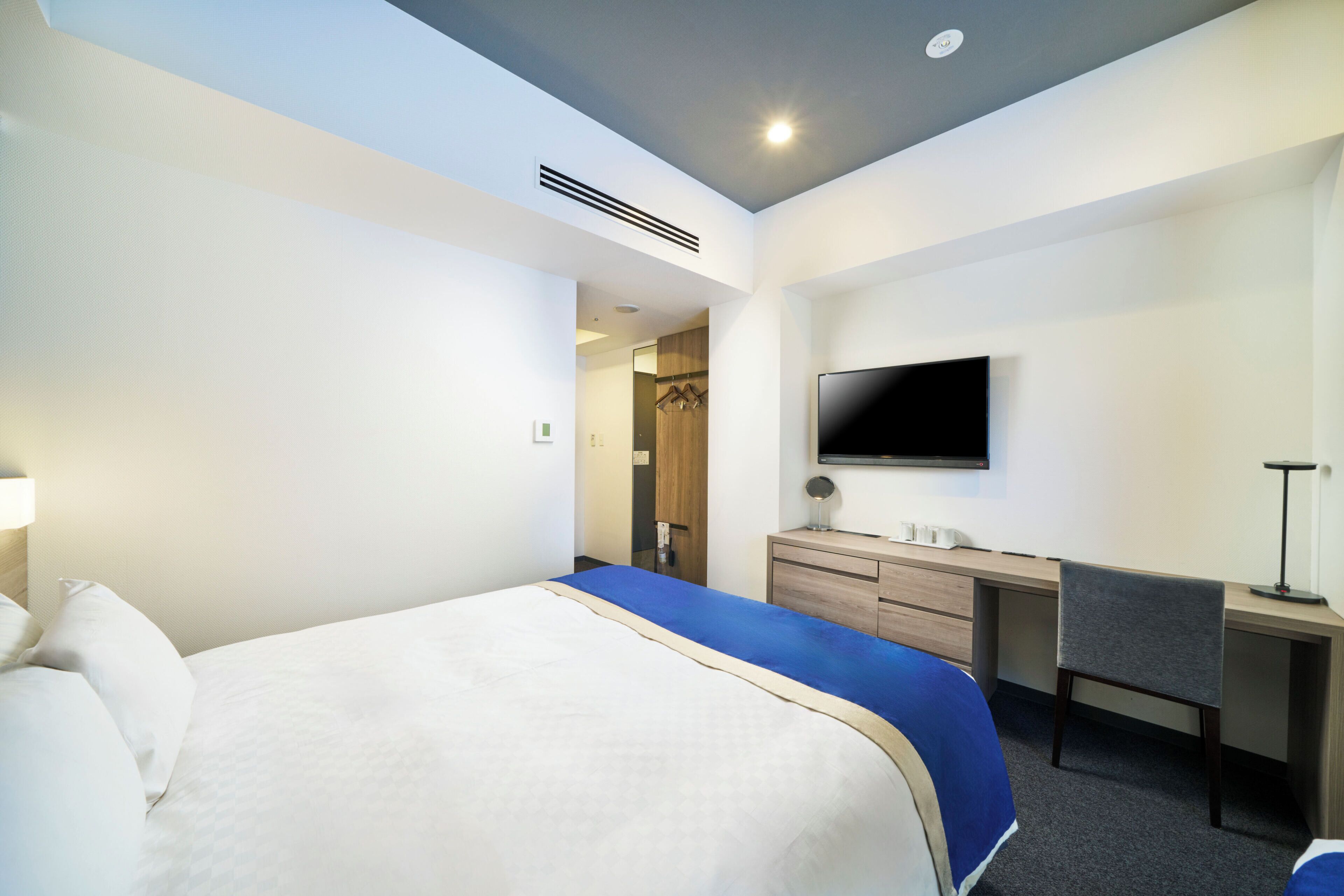Quarto de hotel com uma cama, uma escrivaninha, uma cadeira, uma televisão e um guarda-roupa.