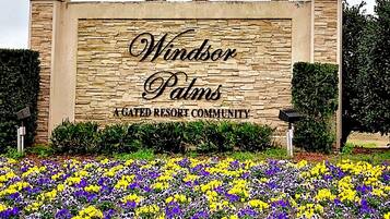 A stone wall with the text 'Windsor Palms A GATED RESORT COMMUNITY' and a flower bed in front.