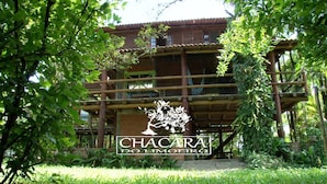 A rustic wooden building with a balcony, surrounded by lush greenery. -  Chacara with incredible house on the edge of the river in Antonina, PR -   (Antonina)