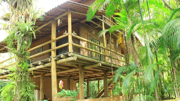 A wooden structure with multiple balconies, surrounded by lush greenery and plants. -  Chacara with incredible house on the edge of the river in Antonina, PR -   (Antonina)
