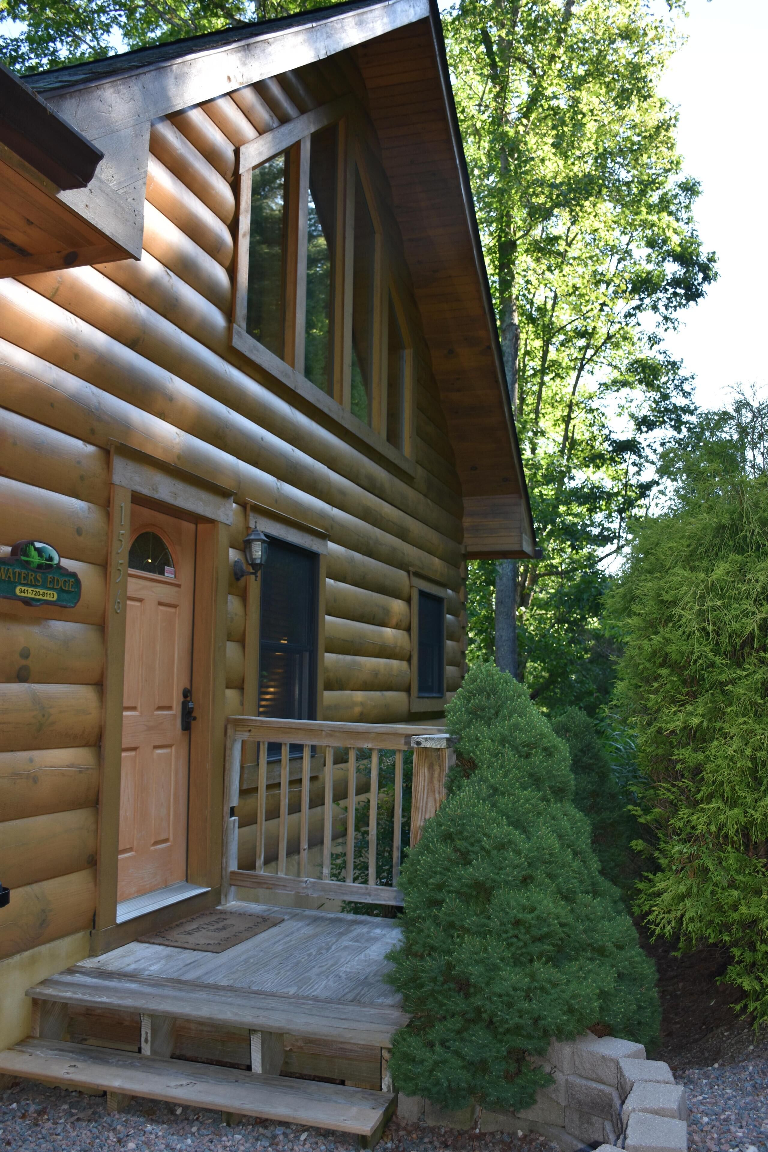 A log cabin with a wooden front door, a small porch, and a sign reading "WATER'S EDGE".