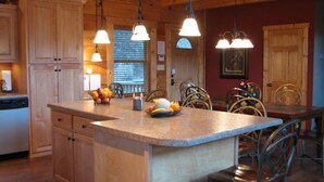A kitchen with wooden cabinets, a granite countertop, and a dining area with metal chairs. - MTN CABIN LAKEFRONT,CANOE/3 KAYAKS,POOL TABLE,DOCK,FIRE PIT, FIREPLACE,JACUZZI (Butler)