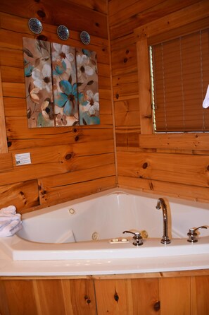 Ein Badezimmer einer Holzhütte mit einer großen Badewanne, Holzwänden und einem Fenster mit Jalousien.