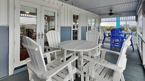 A covered porch with white Adirondack chairs, a round table, and ceiling fans.