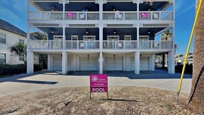 A two-story building with balconies, a sign indicating 'POOL', and a clear blue sky.