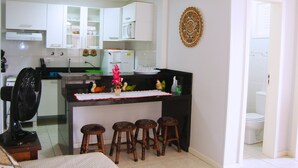 A compact kitchen with white cabinets, a central island with stools, and a small fan. - Inactive ad (capao da canoa)
