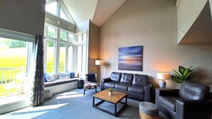 A living room with a sofa, coffee table, and a view of a garden through large windows. - Chalet Style Townhome, Very Clean, Great Condition, Walk to Village, Mtn. Views. (The Blue Mountains)
