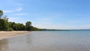 A beach with clear water, trees, and a distant shoreline. - Chalet Style Townhome, Very Clean, Great Condition, Walk to Village, Mtn. Views. (The Blue Mountains)