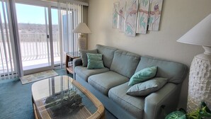 Una sala de estar con un sofá, una mesa de centro de vidrio y un ventanal con vistas.