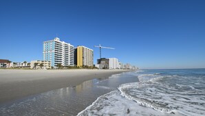 Un hotel frente a la playa con varios pisos, una playa al fondo y una grúa de construcción.