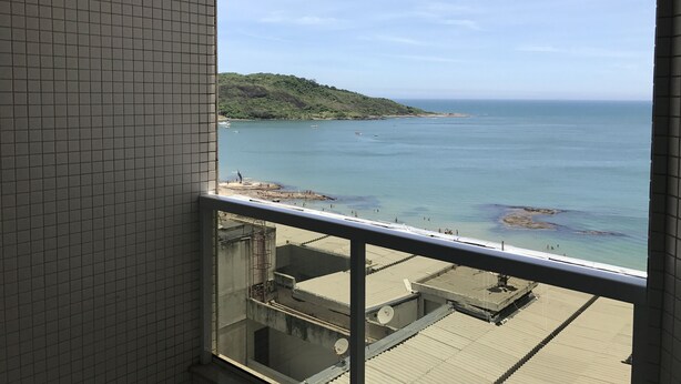 A view from a window overlooking a beach with boats, a hilly landscape, and a clear sky. - Apartment 702B with ocean view, Morro Beach, 3 bedrooms, 2 bathrooms, 1 garage. (Guarapari)