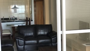 A living room with a black leather sofa, a wooden coffee table, and a kitchen area with a tiled backsplash and a hanging light fixture. - Apartment 702B with ocean view, Morro Beach, 3 bedrooms, 2 bathrooms, 1 garage. (Guarapari)