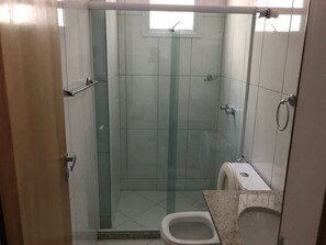 Un baño con cabina de ducha de vidrio, inodoro y lavamanos.