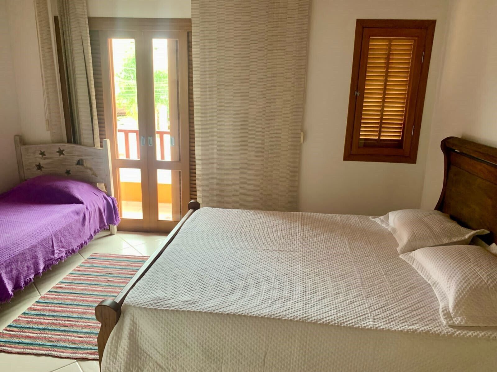 A bedroom with a bed, a window with blinds, a door leading to an outdoor area, and a striped rug.