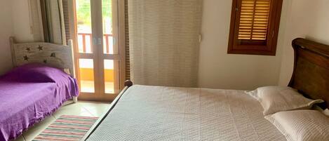 A bedroom with a bed, a window with blinds, a door leading to an outdoor area, and a striped rug.