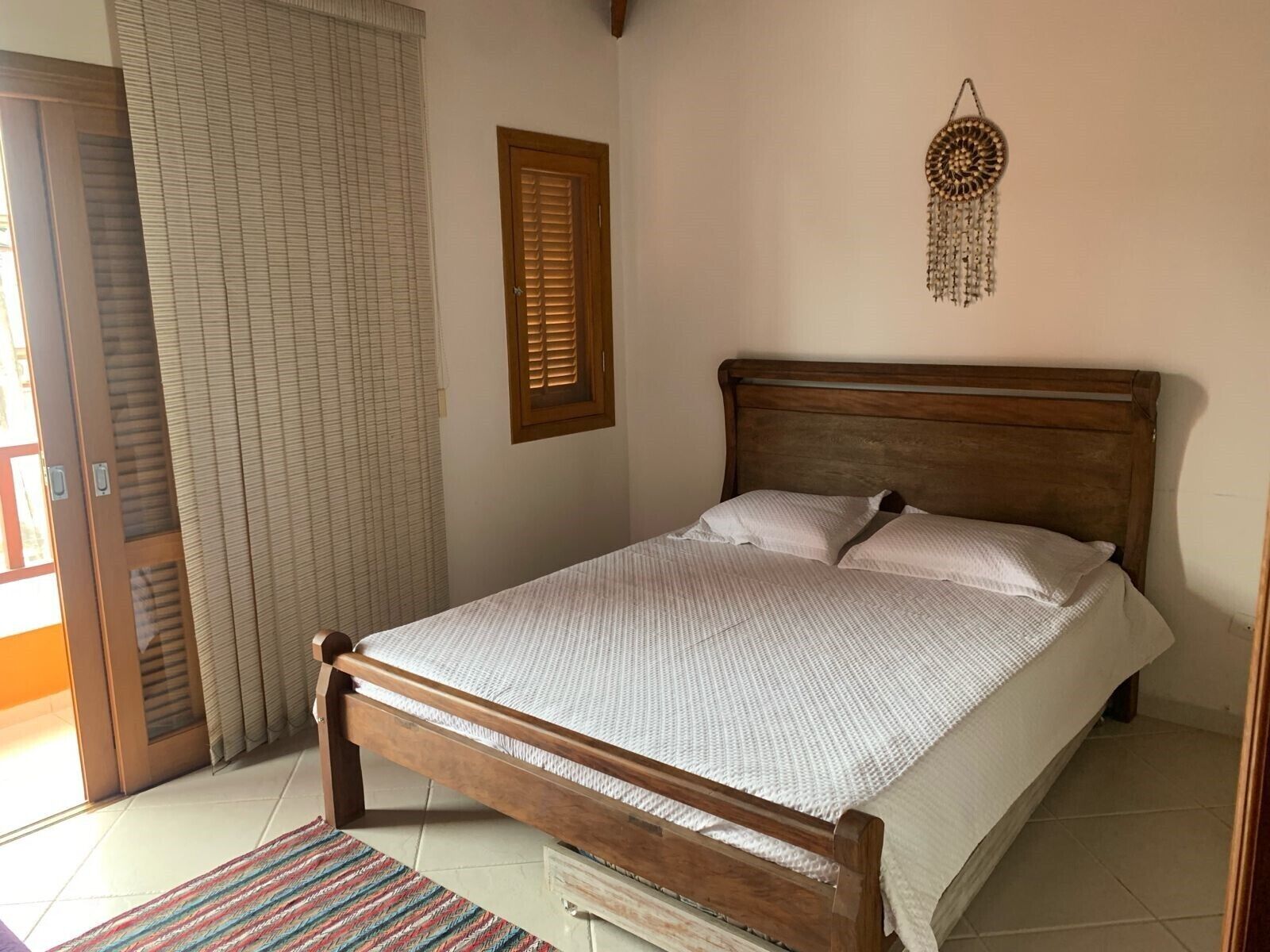 Ein Schlafzimmer mit einem hölzernen Bett, einem Fenster mit Jalousien, einer Tür und einem Wandbild.