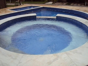 Ein runder Whirlpool mit einer gefliesten Kante, umgeben von einer gefliesten Terrasse.