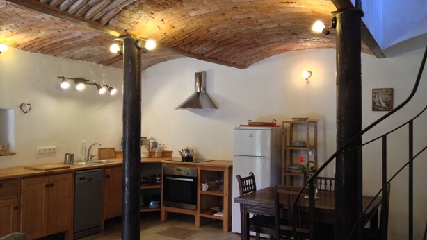 Une cuisine avec un plafond en pierre, des armoires en bois, un four encastré et un coin repas comprenant une table et des chaises.