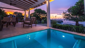 Zona de piscina con sillas y vista al océano al atardecer.