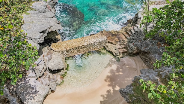 Vista costera con aguas turquesas cristalinas, costa rocosa y vegetación.
