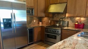 Cocina con gabinetes de madera, electrodomésticos de acero inoxidable y encimera de granito.