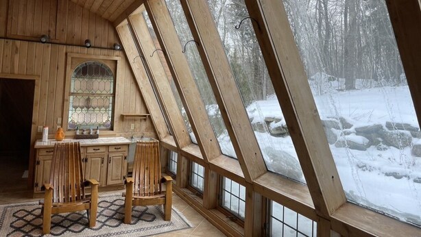 A wooden interior with a kitchen area, large windows, and a view of a snowy landscape. - Snowberry Hill, 5 bedroom, Private Luxury Ski Home on Killington Mtn, sleeps 12 (Killington)