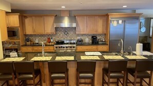 A modern kitchen with wooden cabinets, a stainless steel range hood, a refrigerator, and a central island with bar stools. - Snowberry Hill, 5 bedroom, Private Luxury Ski Home on Killington Mtn, sleeps 12 (Killington)