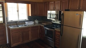A kitchen with wooden cabinets, a stainless steel refrigerator, a microwave, a toaster, and a sink. - Lakeside barn wood cottage just remodeled with all the modern Conveniences! (Greentown, PA)