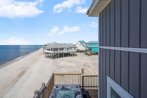 A beachfront property with a wooden deck, a hot tub, and a view of the ocean. - Gulf Front Escape | Hot Tub, Rooftop Views, and Game Room (Dauphin Island)