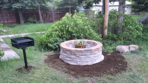 Um jardim com um canteiro circular, uma caixa de correio e vegetação ao redor.