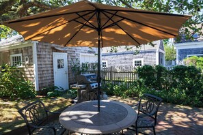 A patio with a round table and chairs, an umbrella, and a grill.