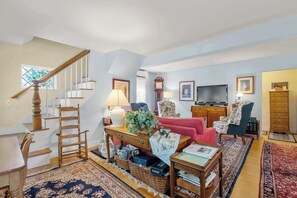 A spacious living room with a staircase, a television, a clock, and a variety of seating options. - On the Chatham Loop - 1 Min to the Beach! (Chatham)