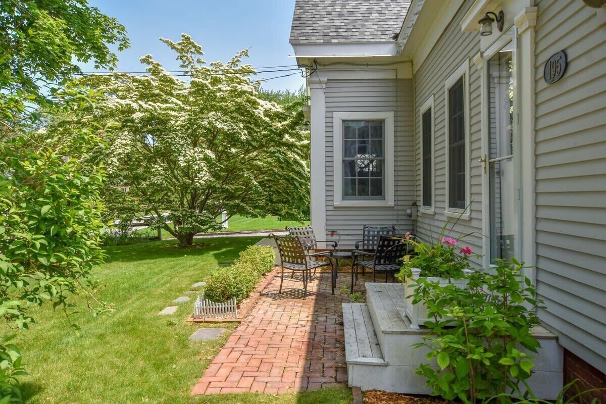 Una casa con un patio de ladrillo, mobiliario exterior y un árbol con flores blancas.
