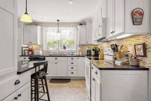 A kitchen with white cabinets, a black countertop, and a window with a view of greenery. - On the Chatham Loop - 1 Min to the Beach! (Chatham)