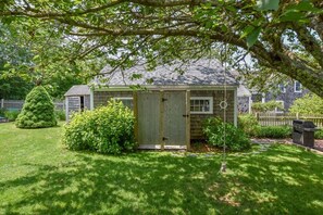 A small wooden shed with a door, surrounded by a well-maintained lawn and a tall tree.
