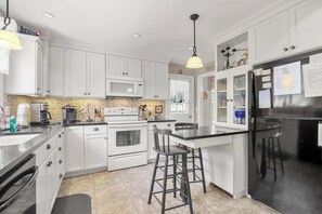 Una cocina moderna con armarios blancos, un refrigerador negro, horno integrado y una zona de comedor con taburetes de bar.