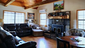 A cozy living room with a fireplace, leather sofas, and a dining table. - Secluded River Cabin Retreat with Outdoor Bathhouse and Kayaks on 80 acres! (Caddo Gap)