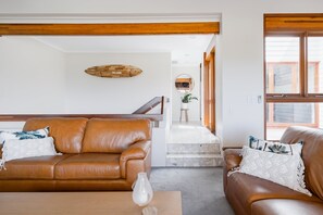 Een moderne woonkamer met twee bruine leren banken, een houten salontafel en een witte vaas. In de achtergrond is een houten plafond en een trap met een spiegel zichtbaar.
