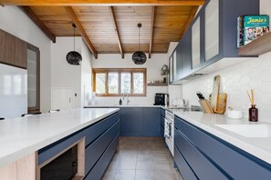 Een moderne keuken met een groot eiland, ingebouwde apparatuur en een houten plafond.