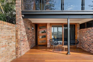 Een modern gebouw met een bakstenen gevel, houten vloeren en een overdekt patio met twee stoelen en een tafel.