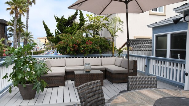 Una terraza con un sofá modular, sillas de mimbre, una mesa redonda y una planta en maceta.