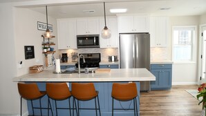 Una cocina moderna con armarios blancos, un refrigerador de acero inoxidable, un microondas y una isla grande con taburetes de bar.