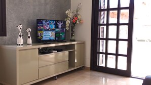 Een televisie op een kast, een vaas met bloemen en een raam met jaloezieën.