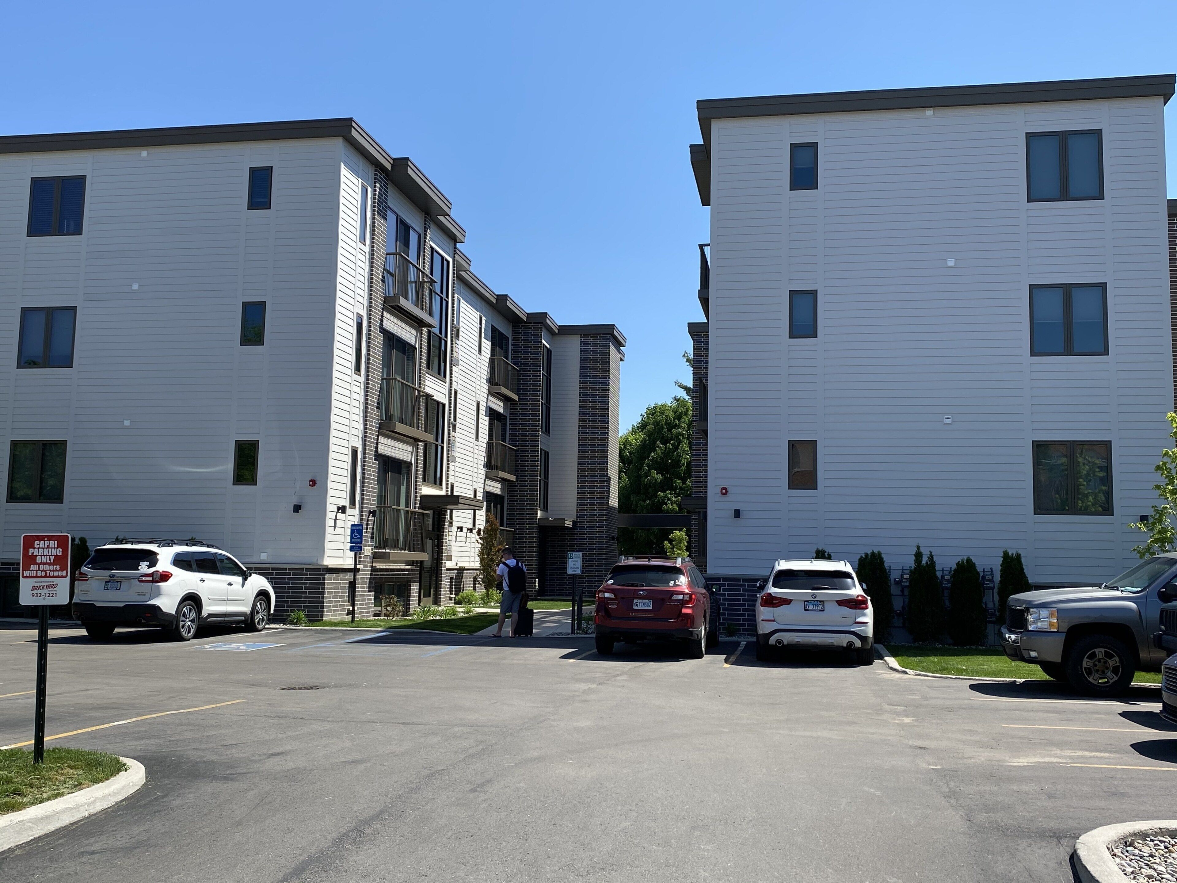 A parking lot with several cars and a person standing near a building.