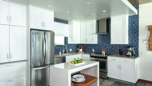 A modern kitchen with white cabinetry, a stainless steel refrigerator, a coffee maker, and a blue-tiled backsplash.