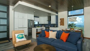 A modern living room with a blue sofa, a wooden chair, and a dining area with a table and chairs.